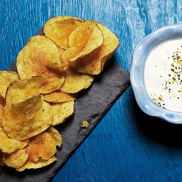 Potato chips on a stone plate, and a light blue bowl with a dip