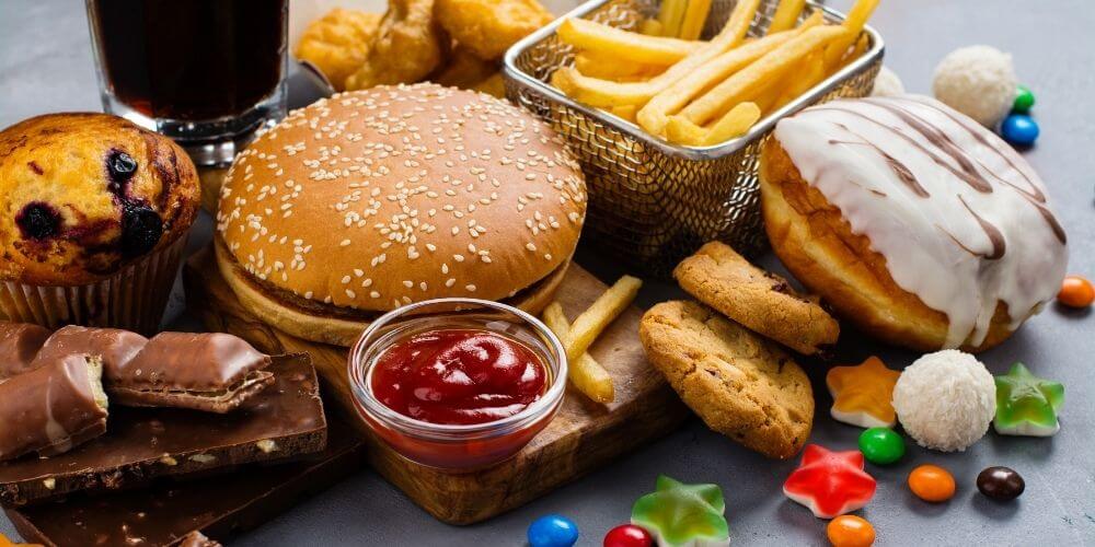 A wooden plate full of fast food (pizza, hamburger, a hot dog, nuggets, french fries, etc.)
